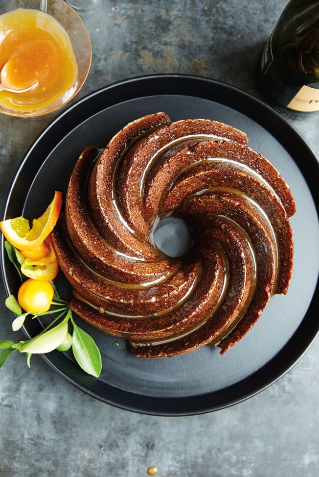 Spiral bundt cake with honey glaze and citrus garnish on a black plate.