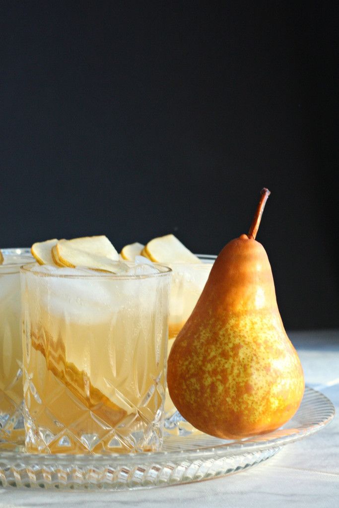 Crystal glasses with pear cocktails and fresh whole pear on a tray against dark background.