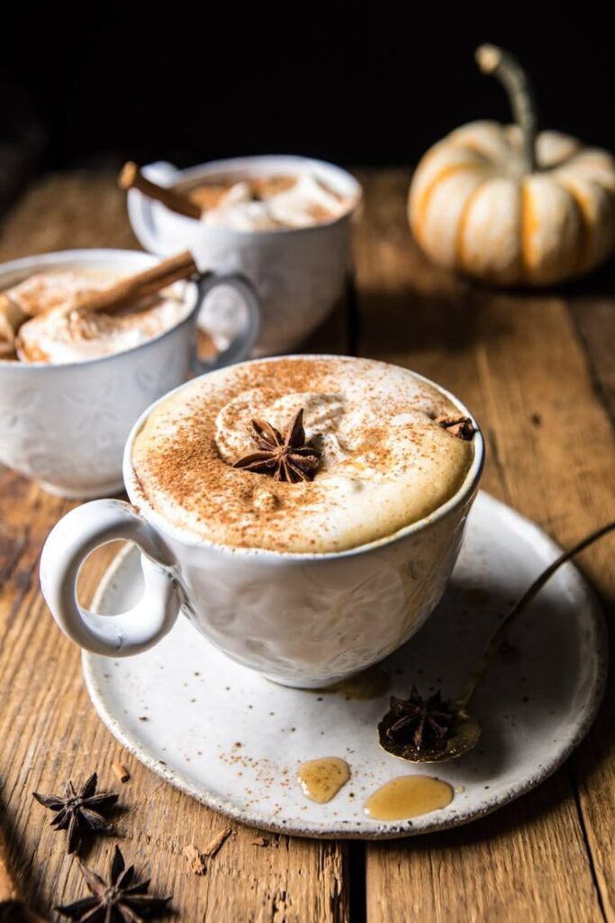 Creamy spiced latte topped with star anise and cinnamon, served on a rustic wooden table with a small pumpkin nearby.