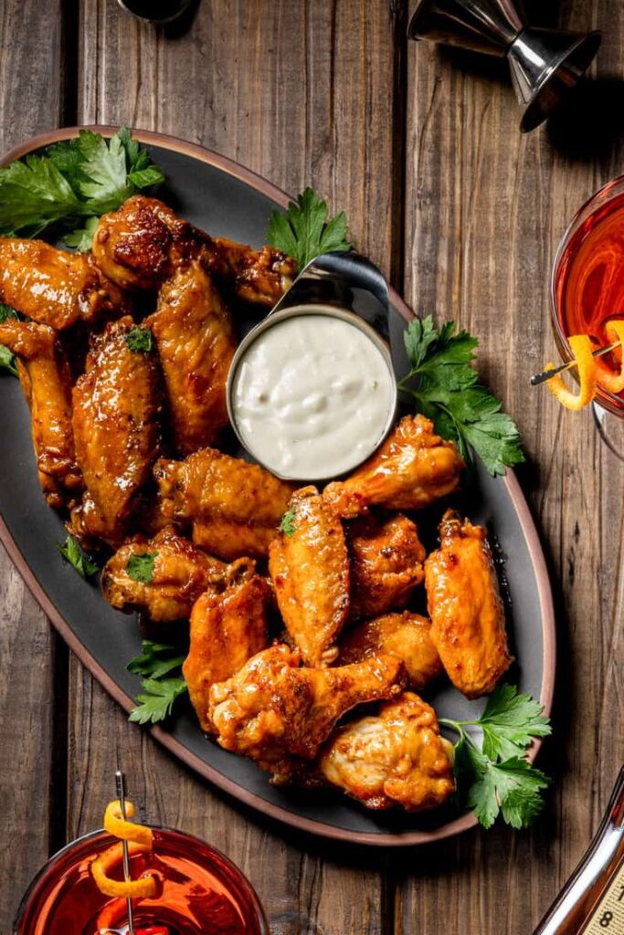 Plate of crispy chicken wings with creamy dipping sauce on a wooden table, garnished with fresh parsley.