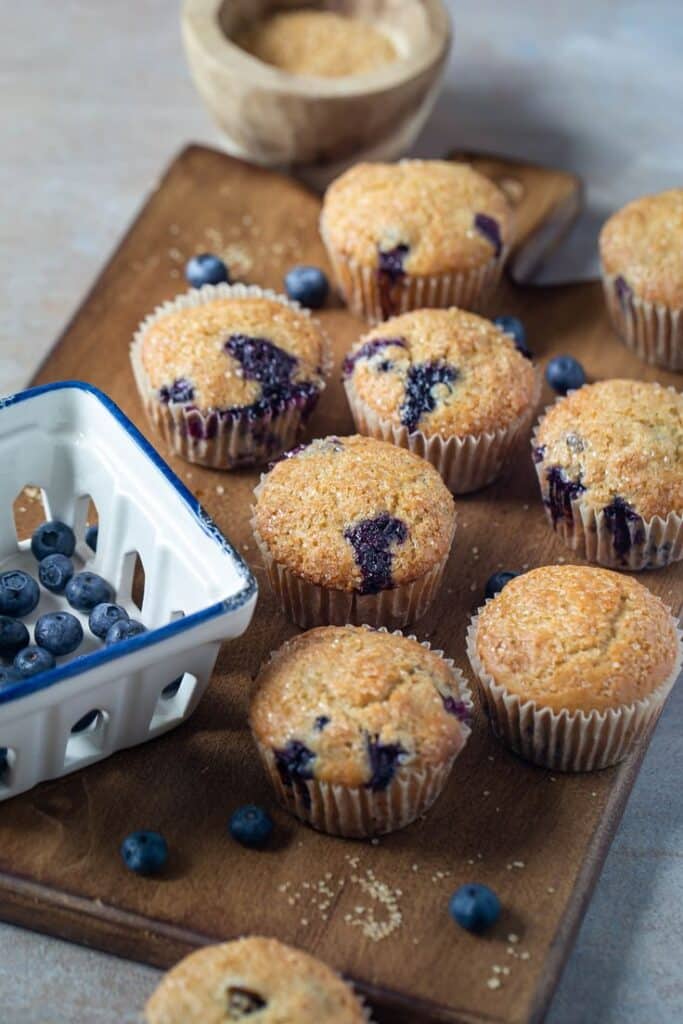 Blueberry muffins on a wooden board with fresh blueberries in a ceramic basket.