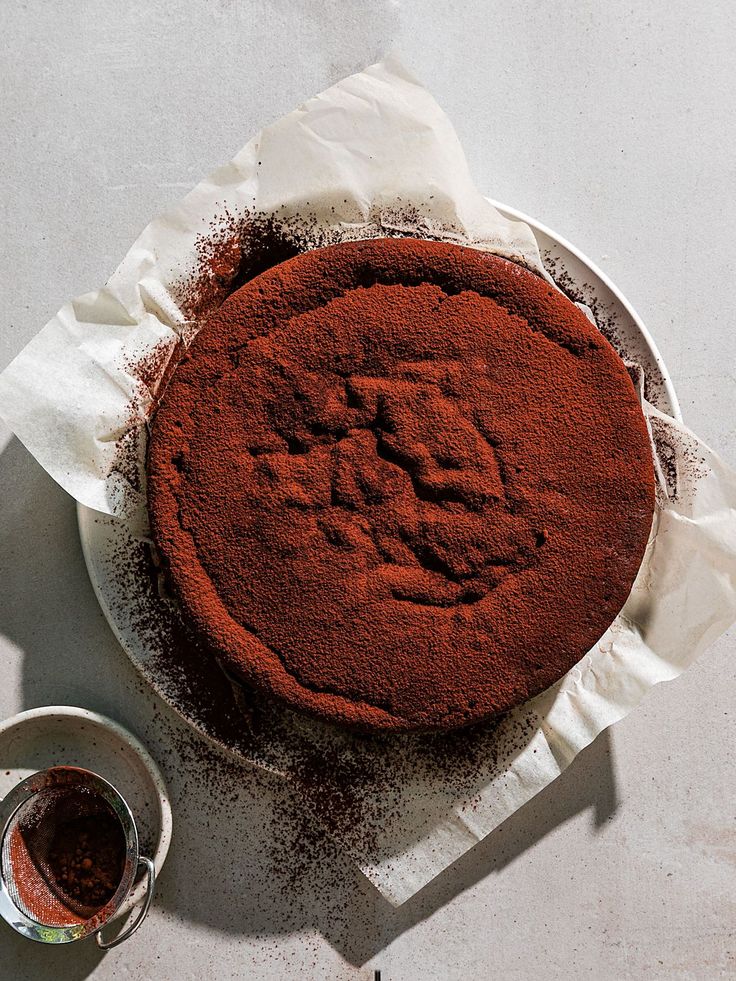 Rich chocolate cake dusted with cocoa powder on parchment paper, on a white plate.