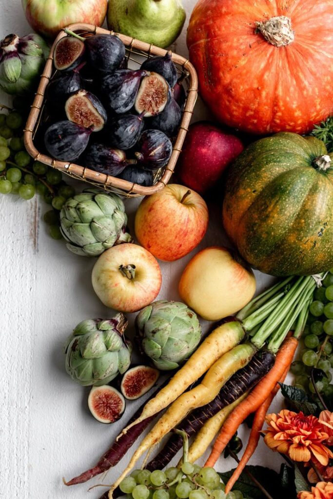 Assorted autumn fruits and vegetables including figs, pumpkins, apples, and carrots on a rustic white table.
