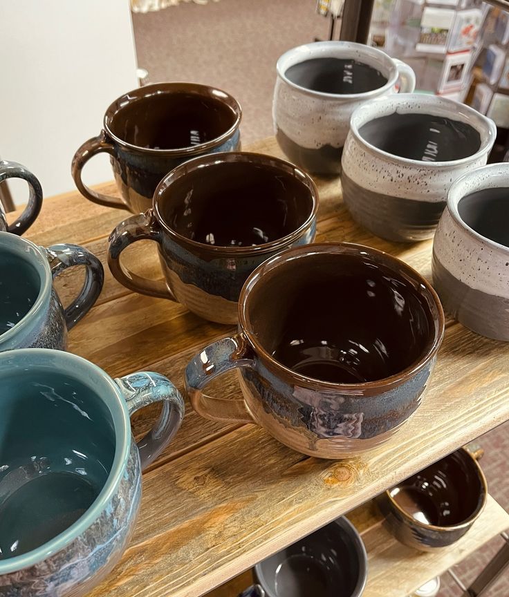 Handcrafted ceramic mugs on a wooden shelf, featuring various earthy tones and glazed finishes.