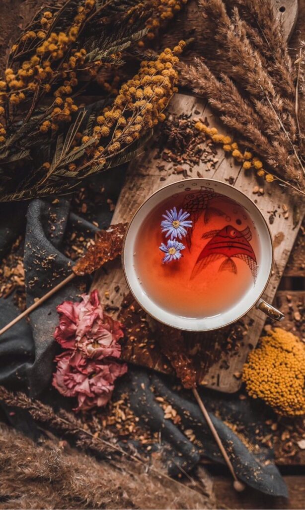 Cup of herbal tea with flowers, surrounded by rustic dried plants and petals, on a wooden board.