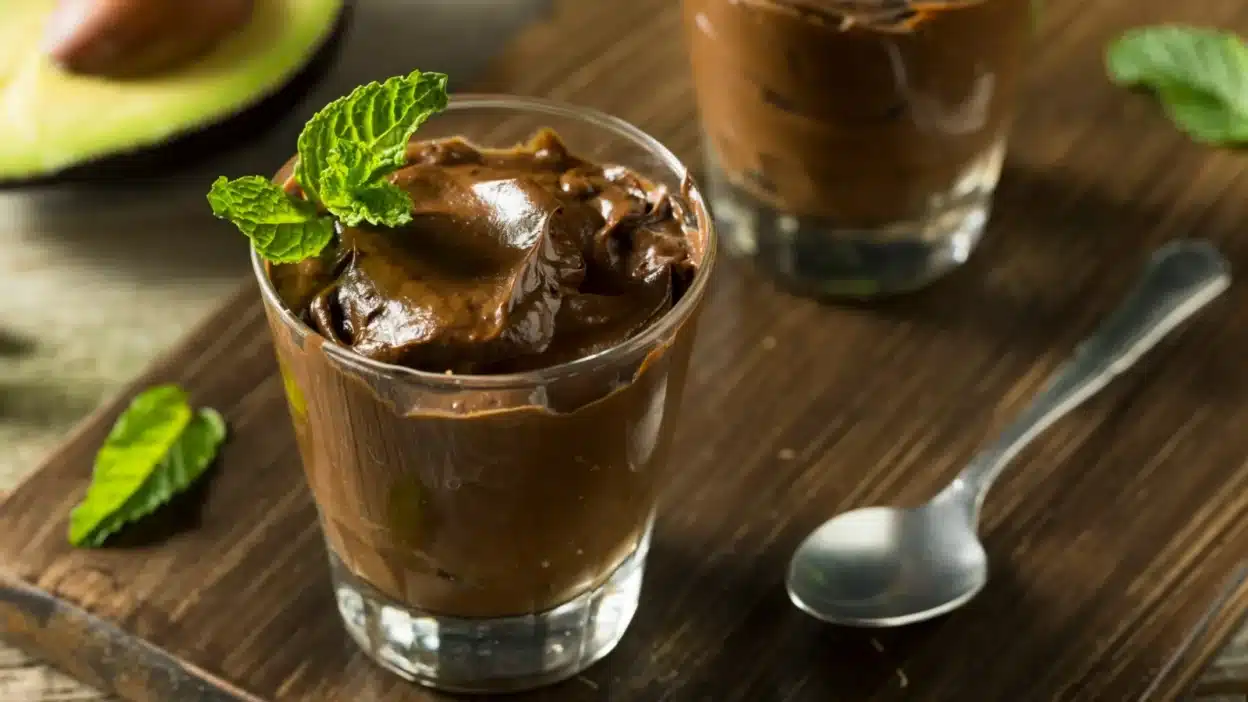 Creamy avocado chocolate mousse garnished with fresh mint in glass cups on wooden table.