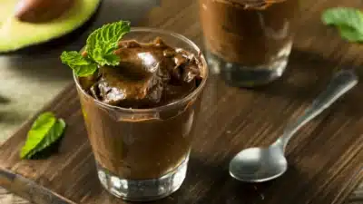 Creamy avocado chocolate mousse garnished with fresh mint in glass cups on wooden table.