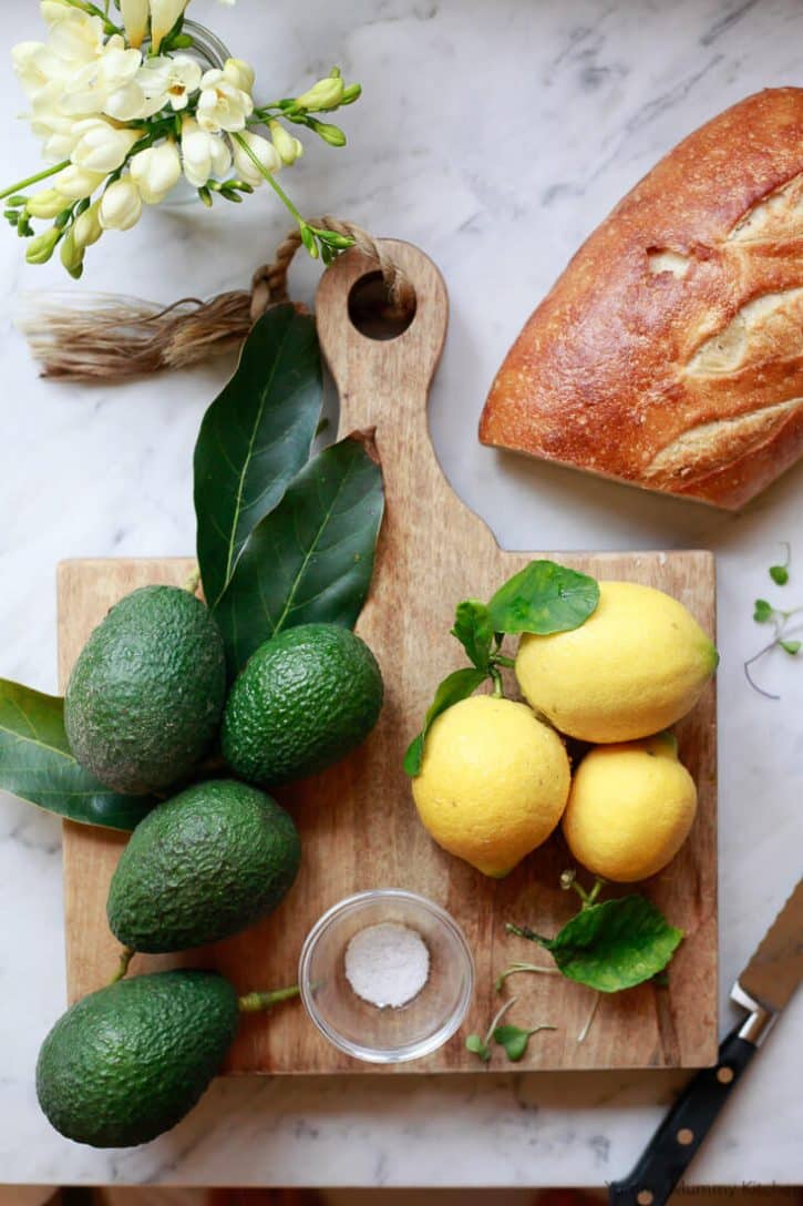 Avocados, lemons, and bread on a wooden board with flowers, perfect for a fresh, homemade meal.