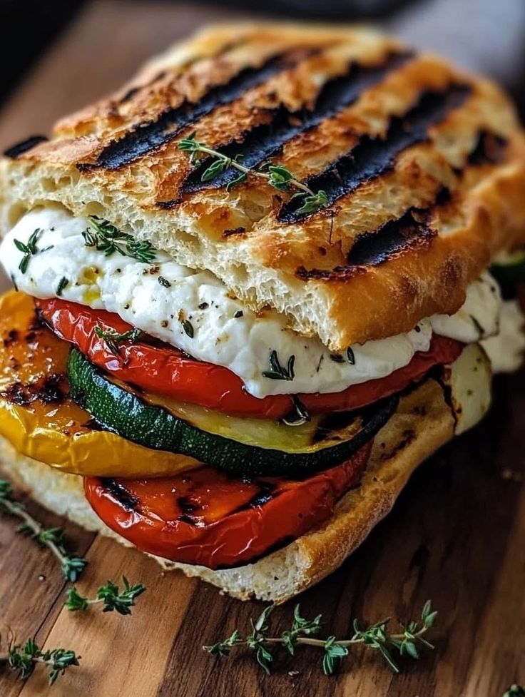 Grilled veggie sandwich with mozzarella, zucchini, peppers, and herbs on toasted bread.