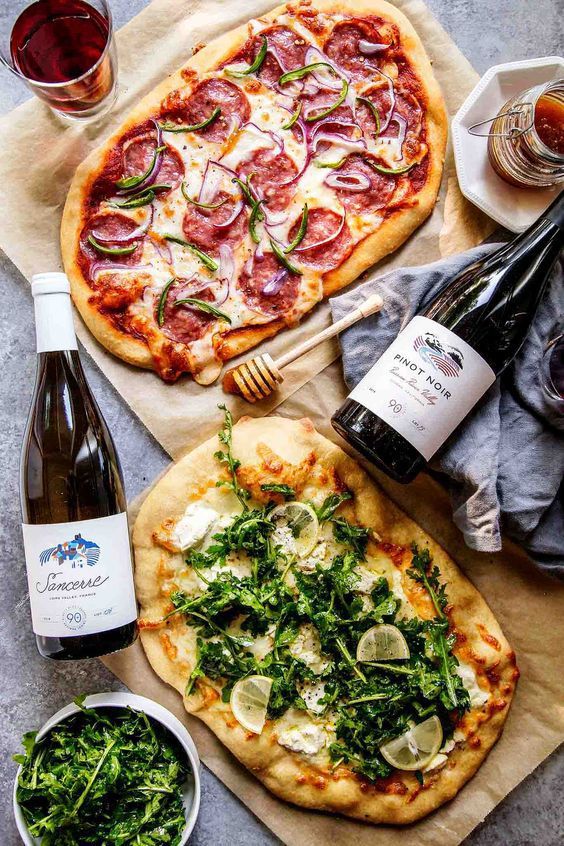 d6fd4862-ce37-475f-a09b-ee27cc357e38 - Master the Art of Homemade Pizza with Fun, Simple Steps | Gourmet pizzas with arugula and salami paired with Pinot Noir and Sancerre wine bottles on rustic parchment.