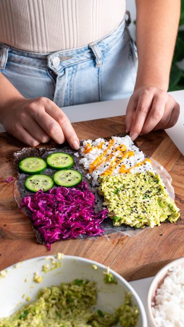 Preparing a vibrant sushi wrap with fresh cucumber, avocado, purple cabbage, and rice on a wooden board.
