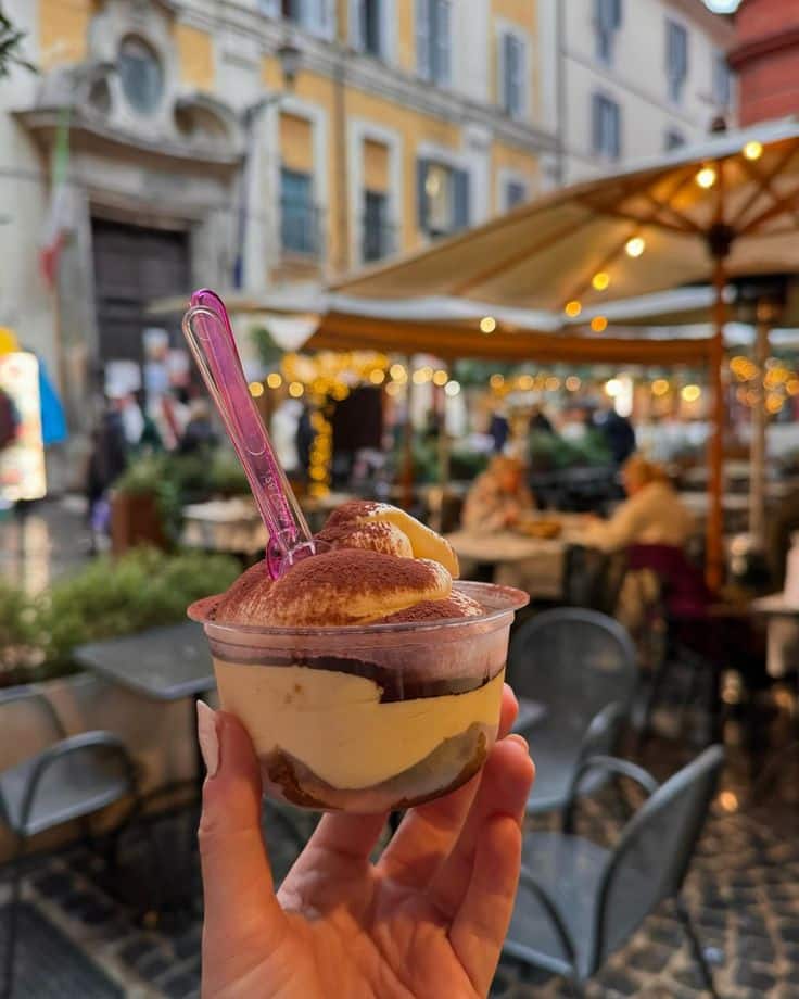 Cup of tiramisu held up in a charming outdoor café setting in Italy.