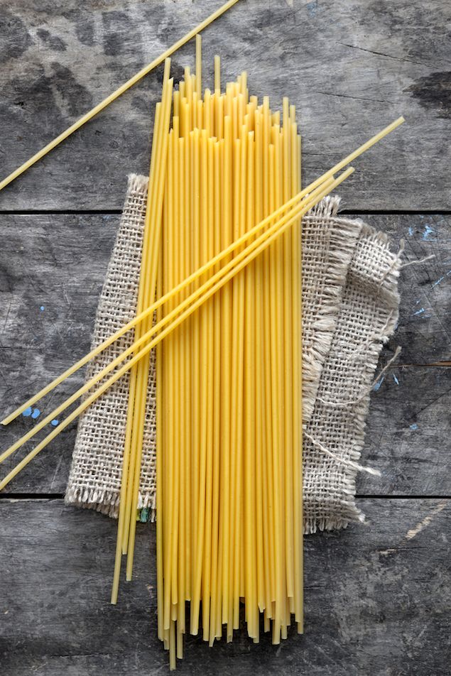 Bundle of uncooked spaghetti on rustic burlap and wooden surface, top view. Perfect for Italian pasta recipes.