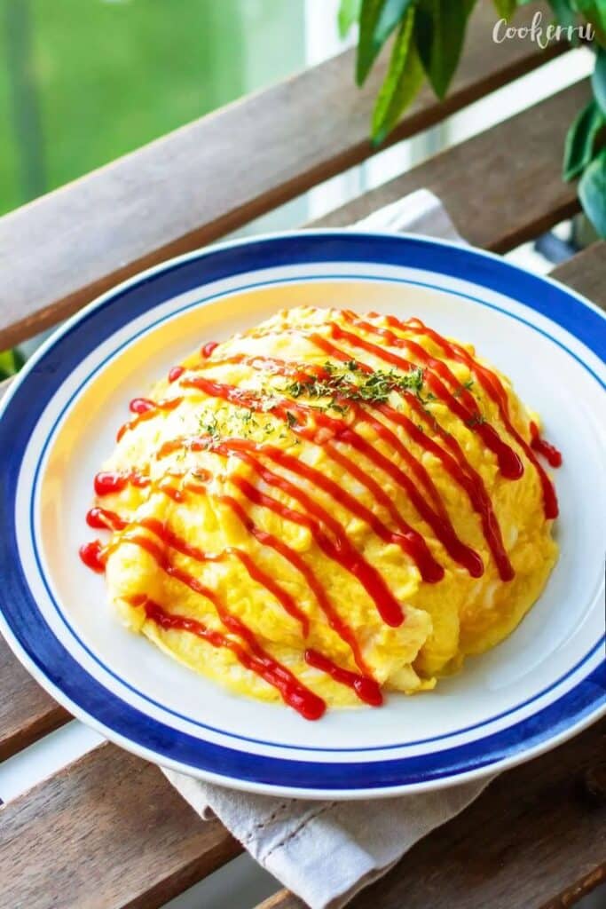 Fluffy omelette rice drizzled with ketchup, garnished with herbs on a plate, on a wooden table.