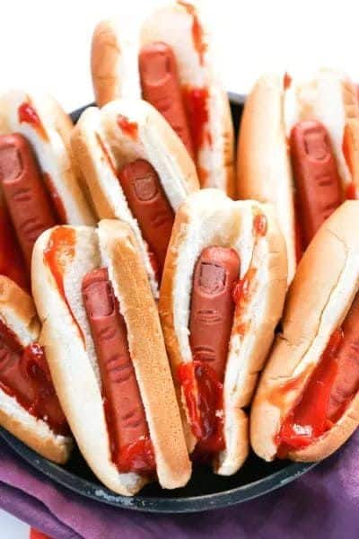 Spooky Halloween hot dogs styled as severed fingers with ketchup in buns. Perfect for a fun, themed party snack.