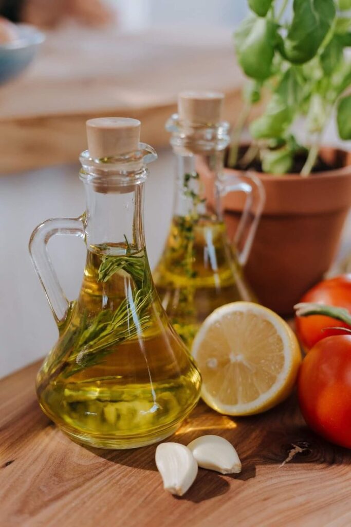 Bottles of infused olive oil with herbs, garlic, lemon, and tomatoes on a wooden table. Perfect for a healthy kitchen vibe.