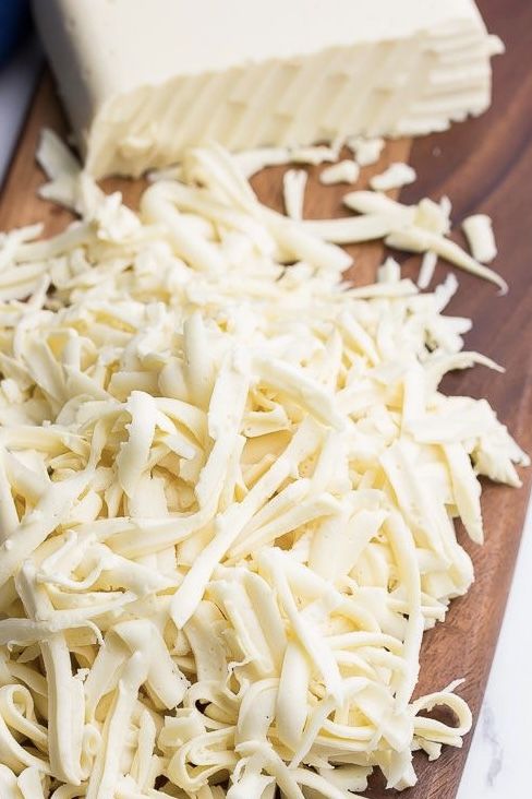 Shredded white cheese on a wooden board, ready for cooking or topping dishes.