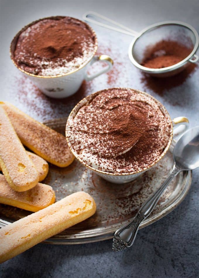 Tiramisu cups with cocoa dusting, served with ladyfingers on a silver tray. Perfect Italian dessert setting.