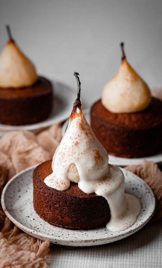Poached pear on chocolate cake with cream drizzle, served on a white speckled plate.