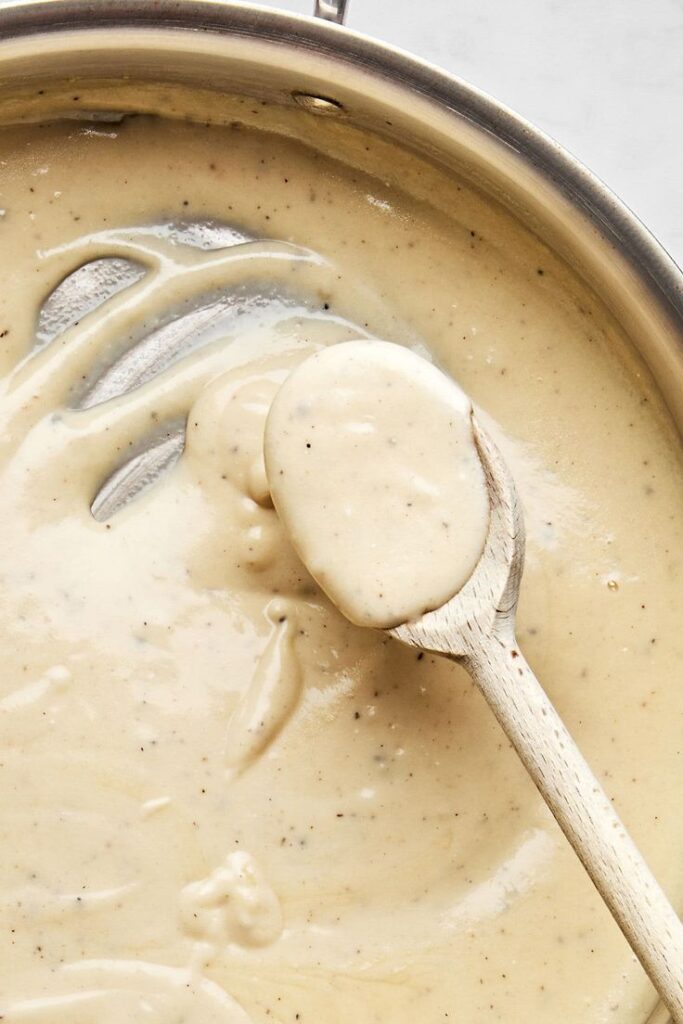 Creamy homemade gravy in a pan with wooden spoon, perfect for adding rich flavor to your dishes.