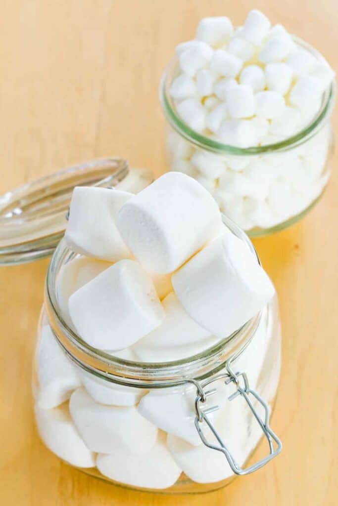 Two glass jars filled with fluffy white marshmallows on a wooden table.
