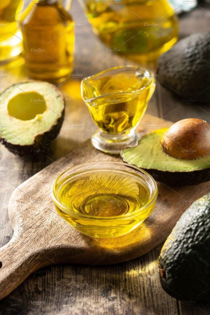 Avocado oil in glass bowls with fresh avocados on a wooden board for healthy cooking concept.