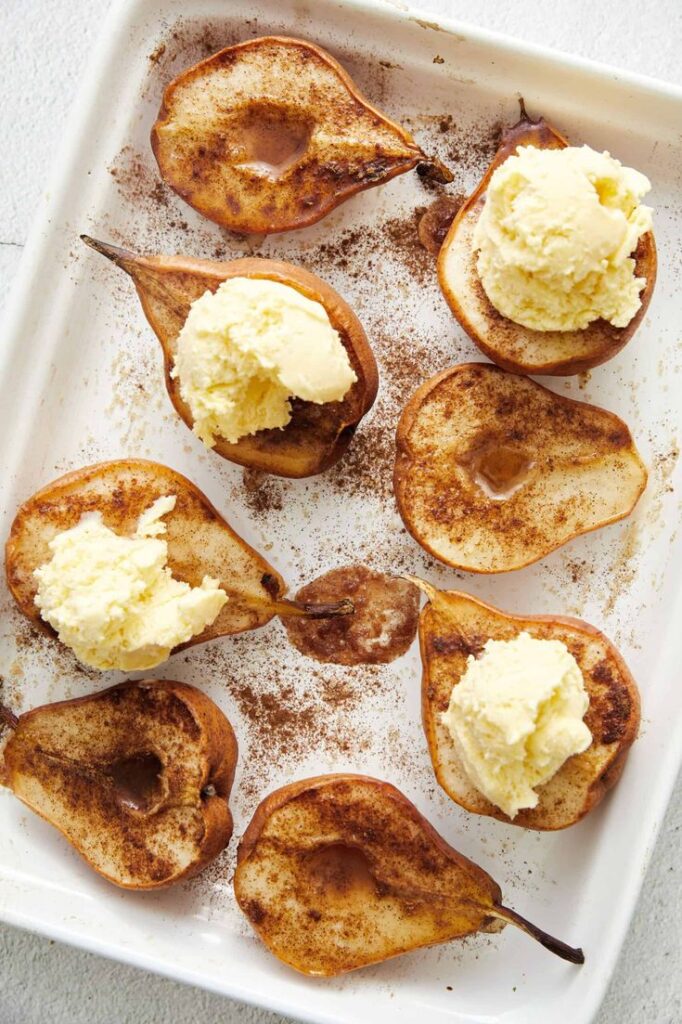 Roasted pears topped with vanilla ice cream and cinnamon on a white tray, a delicious dessert treat.