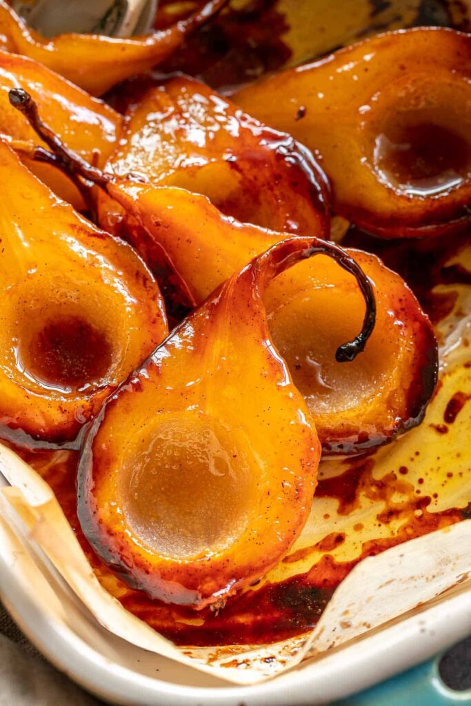Caramelized roasted pears in a baking dish, glistening with syrup and spices, perfect for a dessert or side dish.