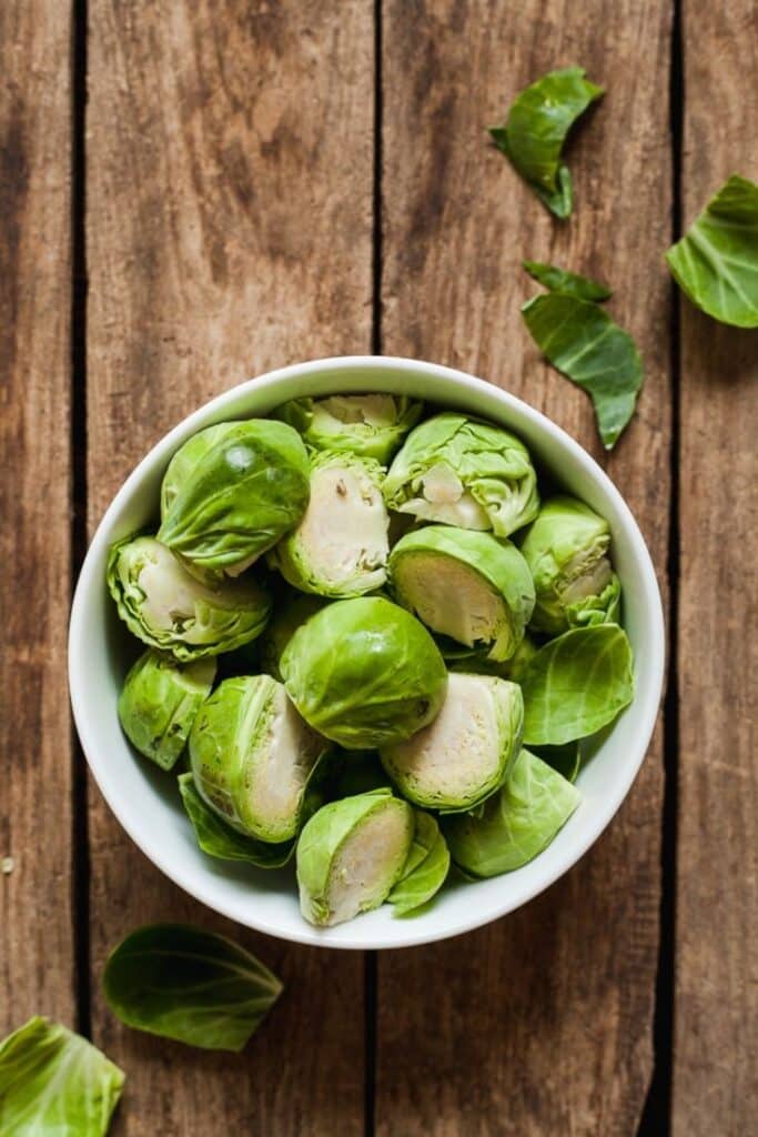 Bowl of fresh Brussels sprouts on rustic wooden table, showcasing vibrant green colors and healthy eating.