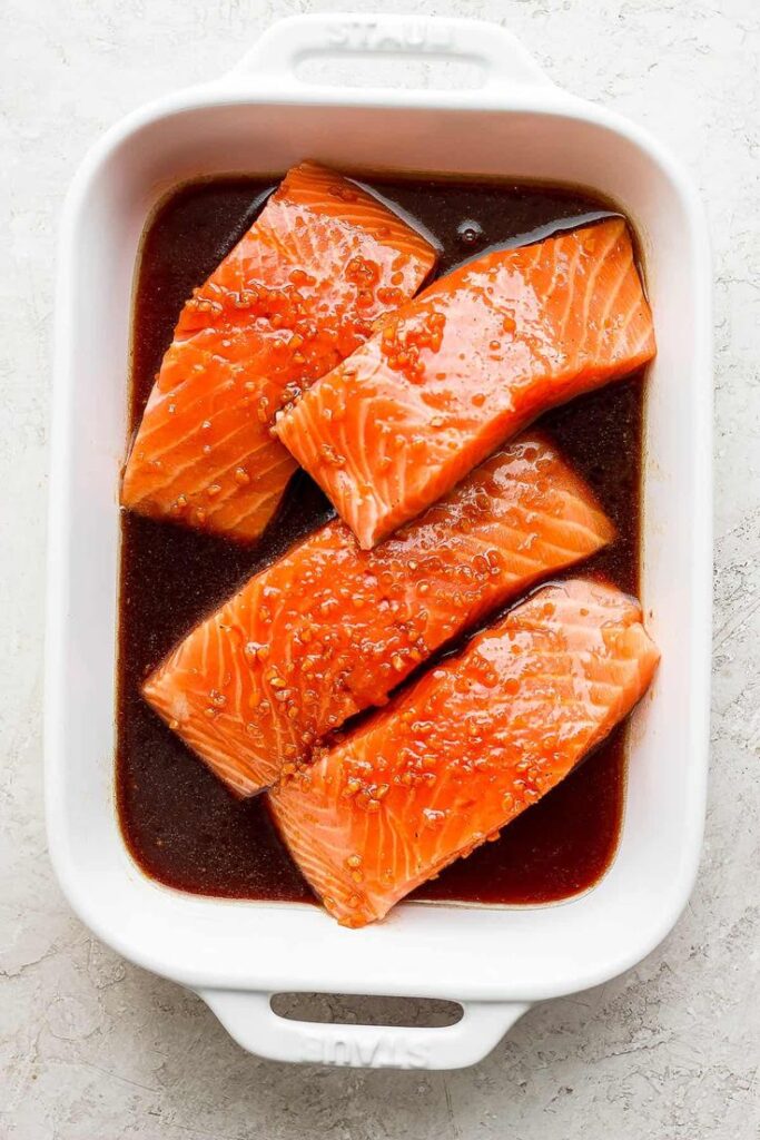Raw salmon fillets marinating in soy sauce glaze in a white baking dish, ready for cooking.