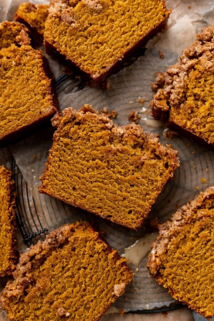 Slices of moist pumpkin bread with crumb topping on parchment paper.