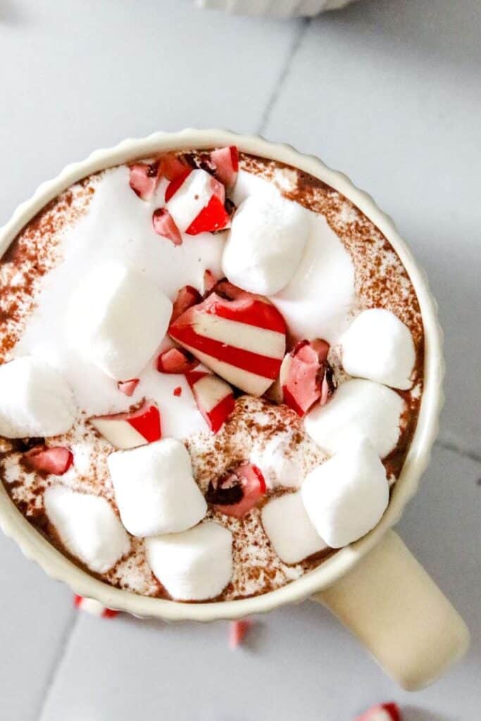 Cup of hot chocolate topped with marshmallows and crushed peppermint candy for a festive treat.