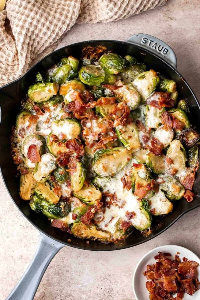 Brussels sprouts with crispy bacon and melted cheese in a black skillet.