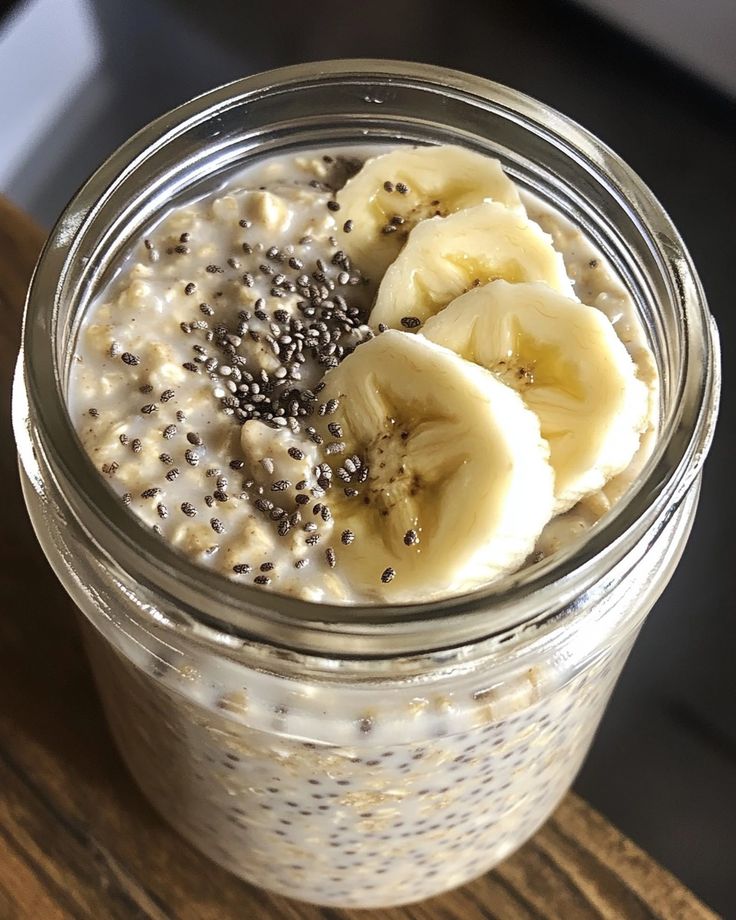 Jar of overnight oats topped with banana slices and chia seeds on a wooden table.
