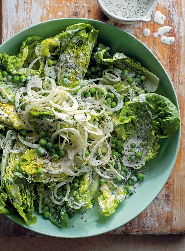 Fresh green salad with lettuce, peas, and onions in a light creamy dressing on a green plate, served on a wooden table.