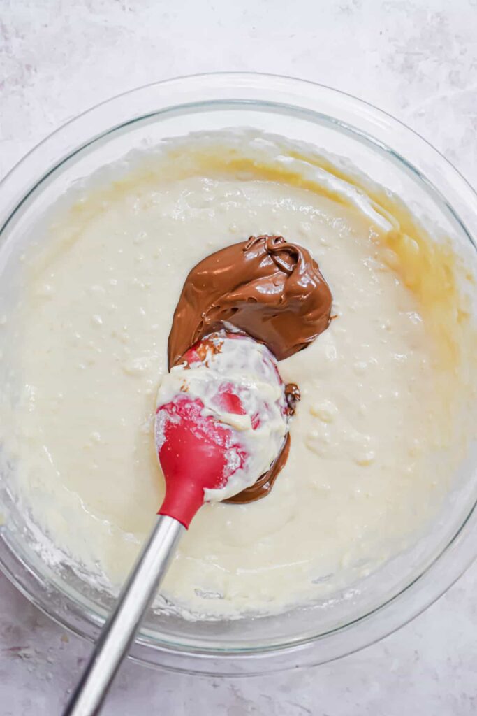 Mixing chocolate and batter in a glass bowl with a red spatula for a delicious dessert preparation.