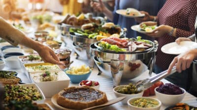 Buffet table with diverse dishes, including salads, seafood, and desserts, and people serving themselves at an event.