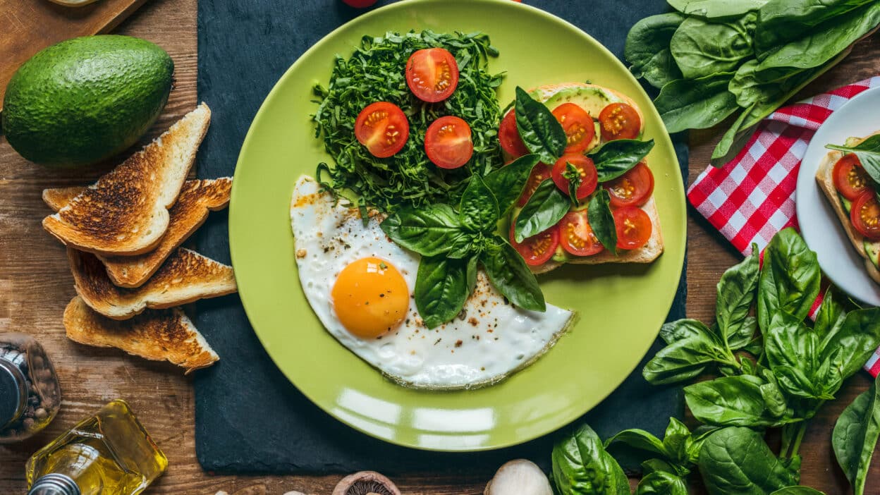 Depositphotos_167638026_XL - Simple, Satisfying Breakfasts for Every Taste and Schedule | Healthy breakfast plate with fried egg, toast, avocado, cherry tomatoes, and greens on a wooden table.