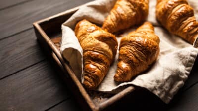 Freshly baked croissants in a wooden tray on a dark wooden table, wrapped in a cloth, ready to serve.