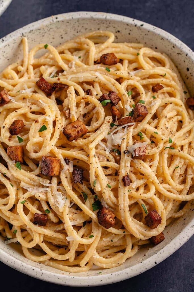 Creamy pasta carbonara with crispy bacon and parsley garnished in a speckled bowl.