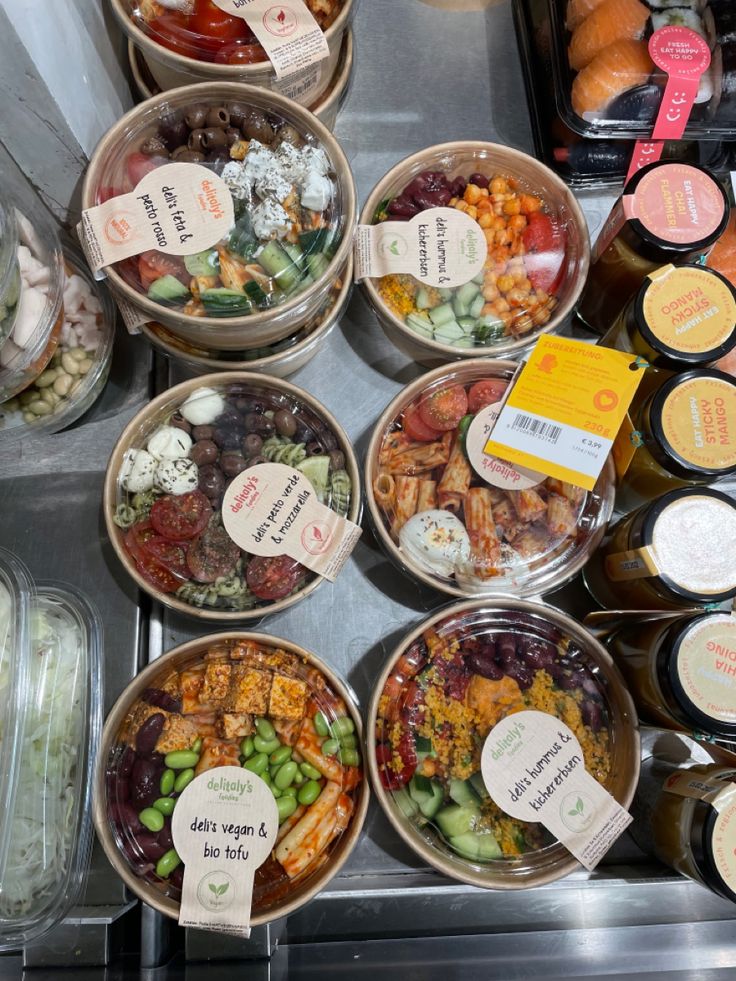 Assorted deli bowls with fresh ingredients like tofu, pasta, and veggies displayed in a grocery store.