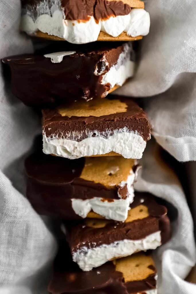 Stack of chocolate-covered marshmallow sandwiches on a cloth, offering a tempting sweet treat.