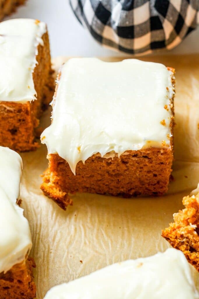 Close-up of a frosted carrot cake square with creamy white icing on parchment paper.
