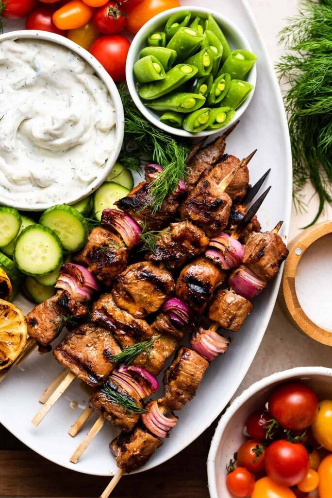 Grilled meat skewers with vegetables, dip, and tomatoes on a platter ready for serving.