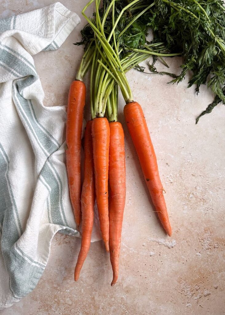 Fresh organic carrots with green tops on a kitchen counter next to a striped cloth.