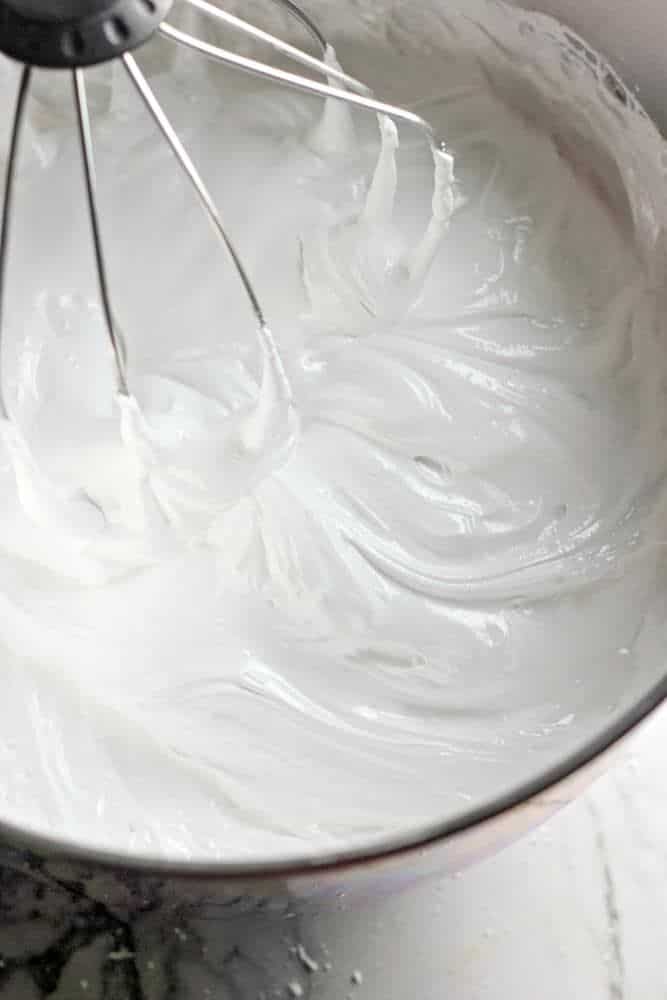 Whipped cream being mixed in a metal bowl with a whisk attachment, showing soft peaks. Perfect for desserts.