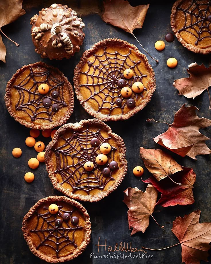 Halloween pumpkin pies with chocolate spiderwebs and candy eyes, surrounded by autumn leaves.