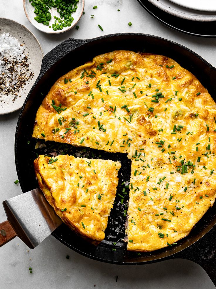 Golden frittata with chives in a cast iron skillet, slice being served. Perfect breakfast dish.