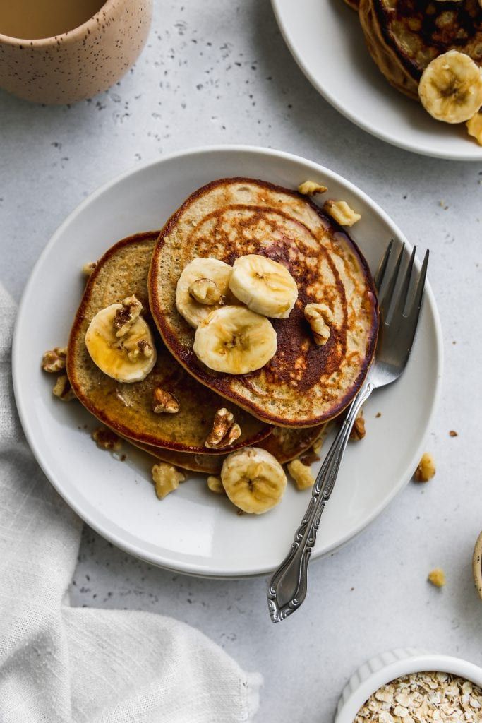 Stack of banana pancakes topped with sliced bananas and walnuts on a plate with a fork, perfect for breakfast.