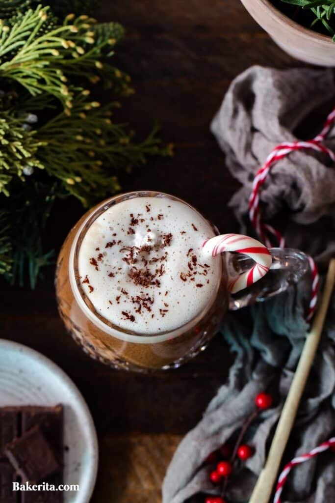 Festive hot chocolate with whipped cream, chocolate shavings, and a candy cane garnish on a wooden table.